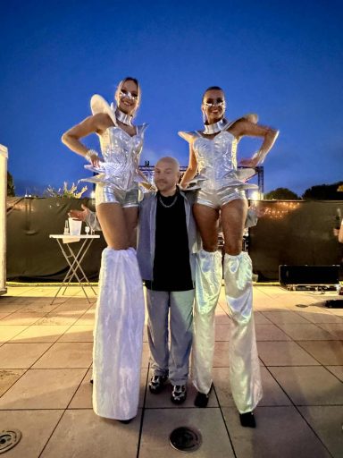 Echassières festival avec Quentin MOSIMANN Deux artistes sur échasses avec un homme au centre, lors d'un événement en soirée.